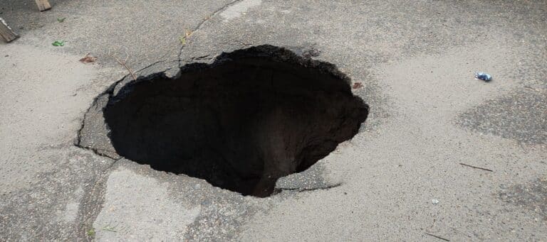 A deep sinkhole with dark soil visible on a damaged road surface