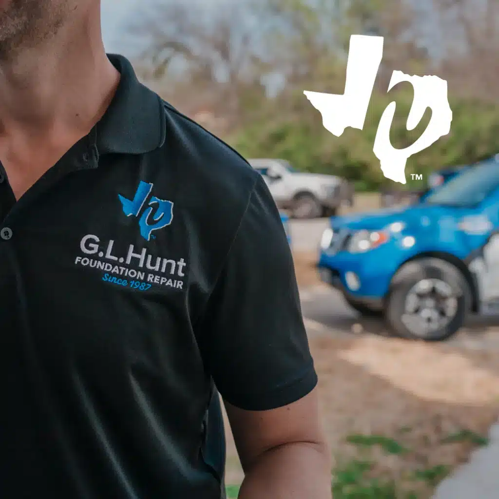Close-up of a G.L. Hunt Foundation Repair technician's uniform with the company logo visible, and a branded truck in the background