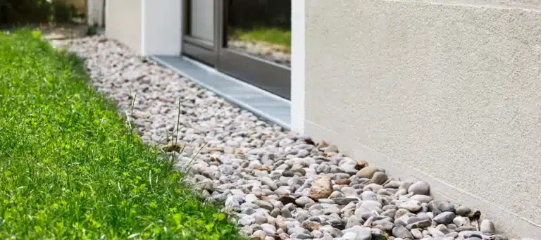 Gravel drainage area next to a house foundation with green grass along the side