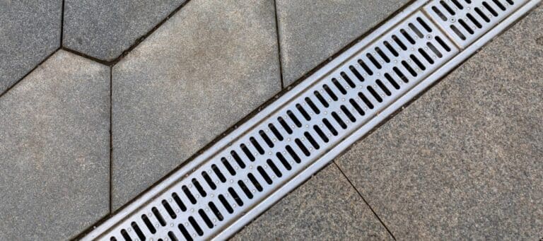 Close-up of a metal drainage grate installed on a stone pathway