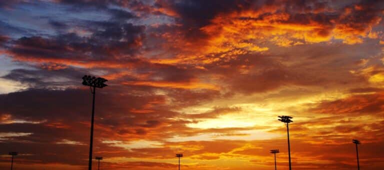 Vibrant sunset sky with dramatic clouds and silhouetted stadium lights