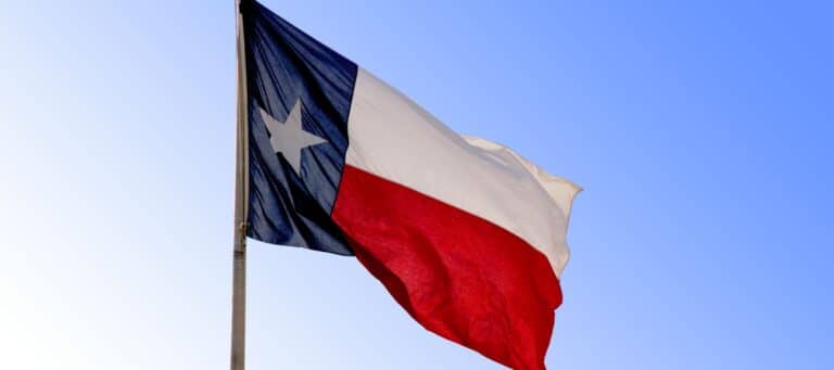 The Texas state flag waving against a clear blue sky