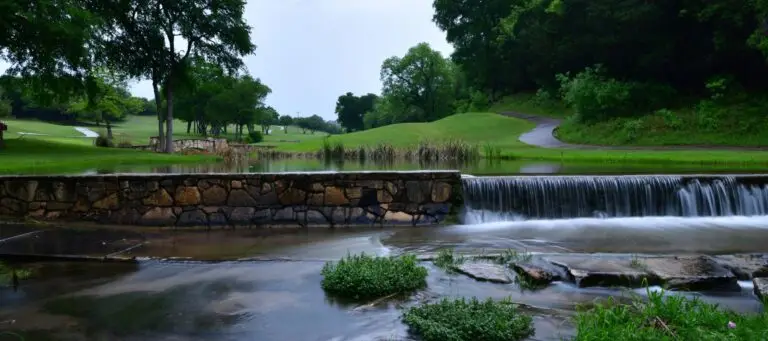 Small stone waterfall flowing through a peaceful park surrounded by trees and walking paths