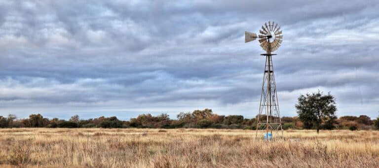 Lone windmill standing in a grassy field under a cloudy sky in rural Texas