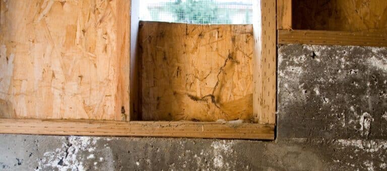 Close-up of a damaged wooden foundation supported by concrete, showing signs of wear and structural issues