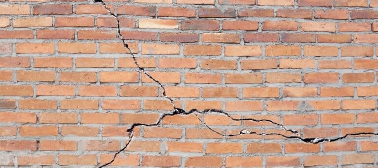 A close-up image of a red brick wall with a large horizontal and vertical crack, indicating structural damage