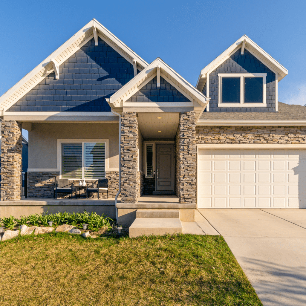 Modern suburban home with stone accents, a covered porch, and a well-maintained front yard under a clear blue sky