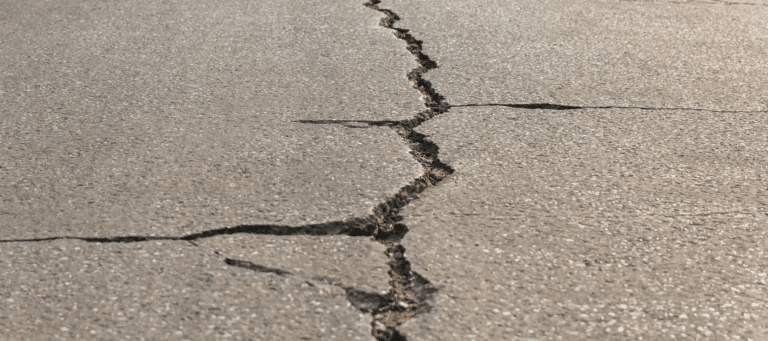 A long, deep crack in a concrete pavement, showing signs of settlement and potential instability