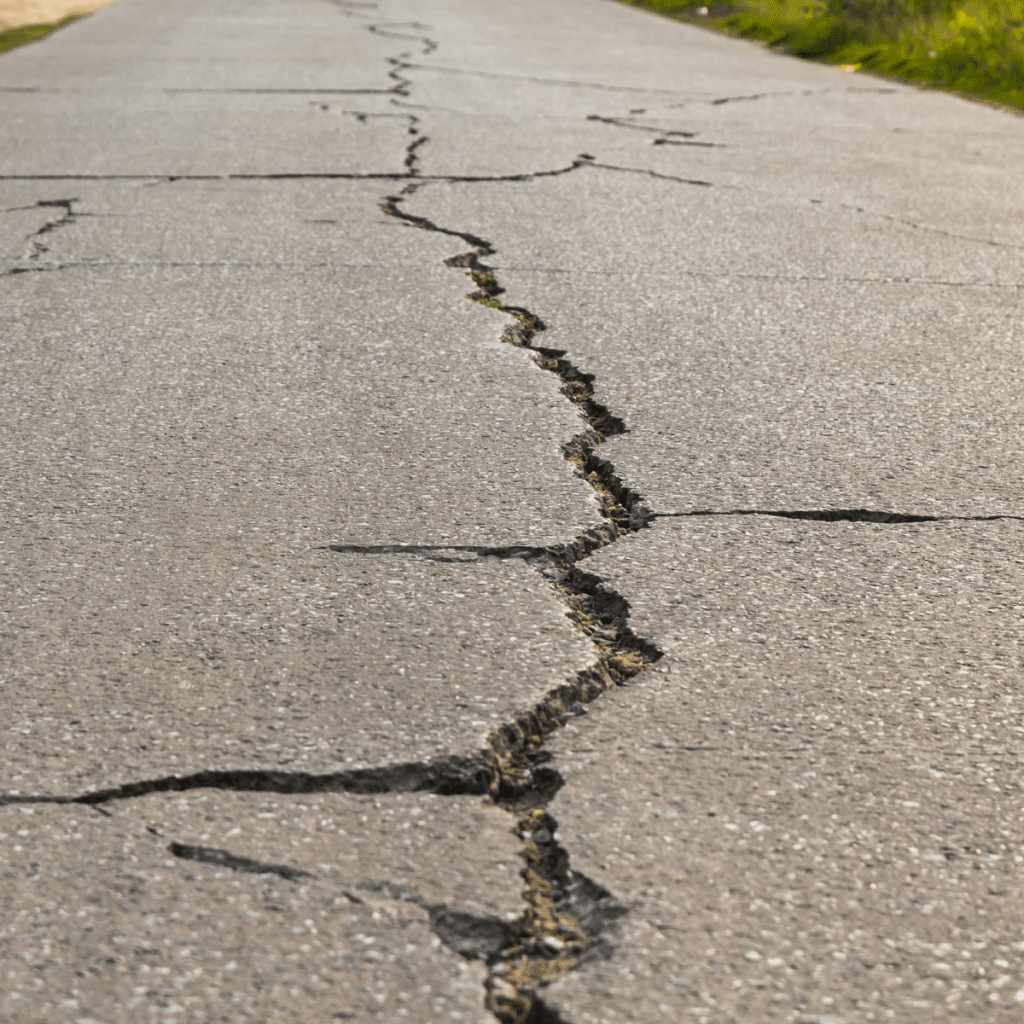 A long, deep crack in a concrete pavement, showing signs of settlement and potential instability