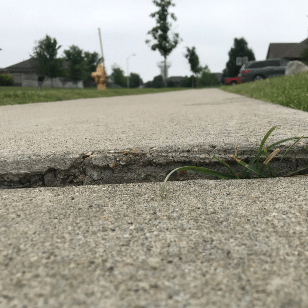 Close-up of an uneven sidewalk with grass growing in a crack