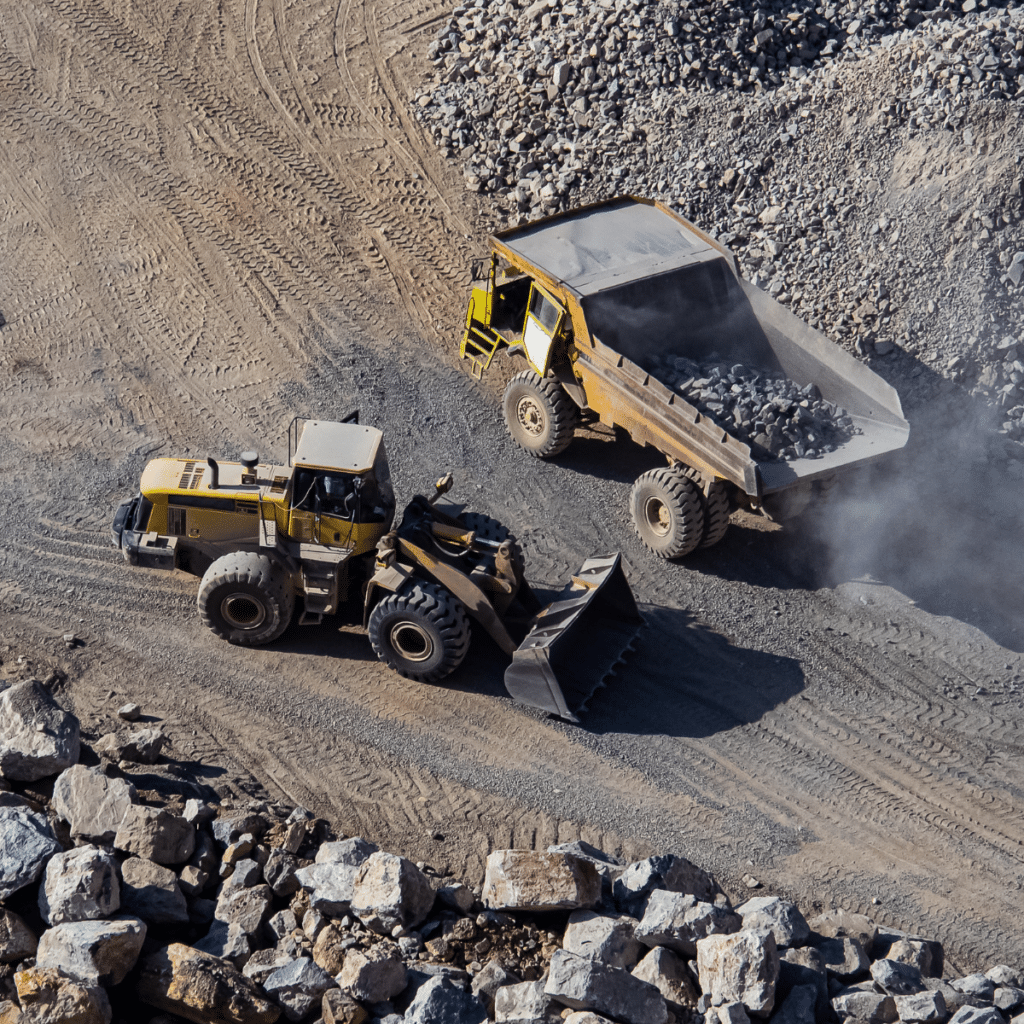 Front loader and dump truck working together at a quarry site, surrounded by piles of rocks and dirt