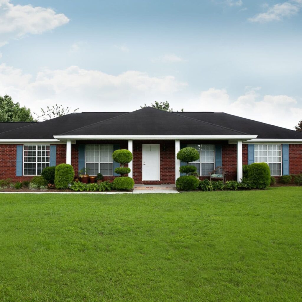 One-story red brick home with blue shutters and manicured front lawn