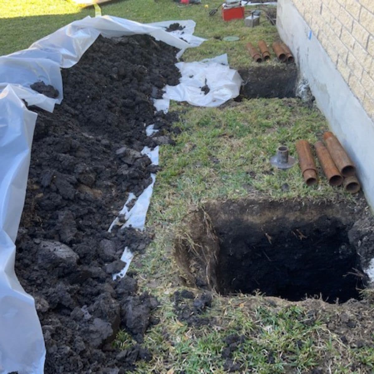 Exposed foundation area with dug holes and piping laid out for repair work