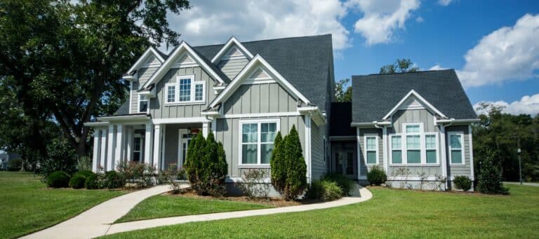 A stately gray and white home with a steep roofline, large windows, and a curved walkway leading to the entrance