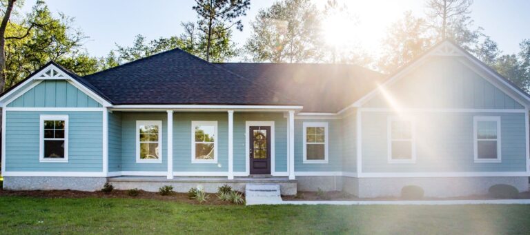 Blue ranch-style house with white trim and sunlight streaming through trees