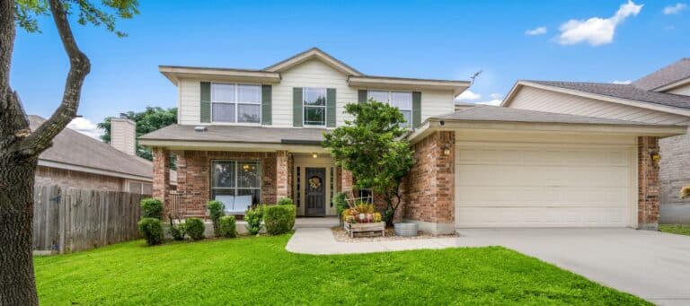 A classic two-story brick home with green shutters, a covered front porch, and a well-maintained front yard