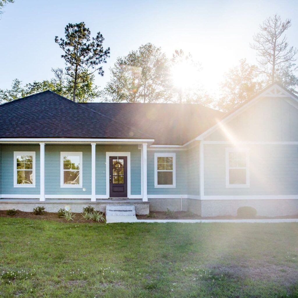 Blue ranch-style house with white trim and sunlight streaming through trees