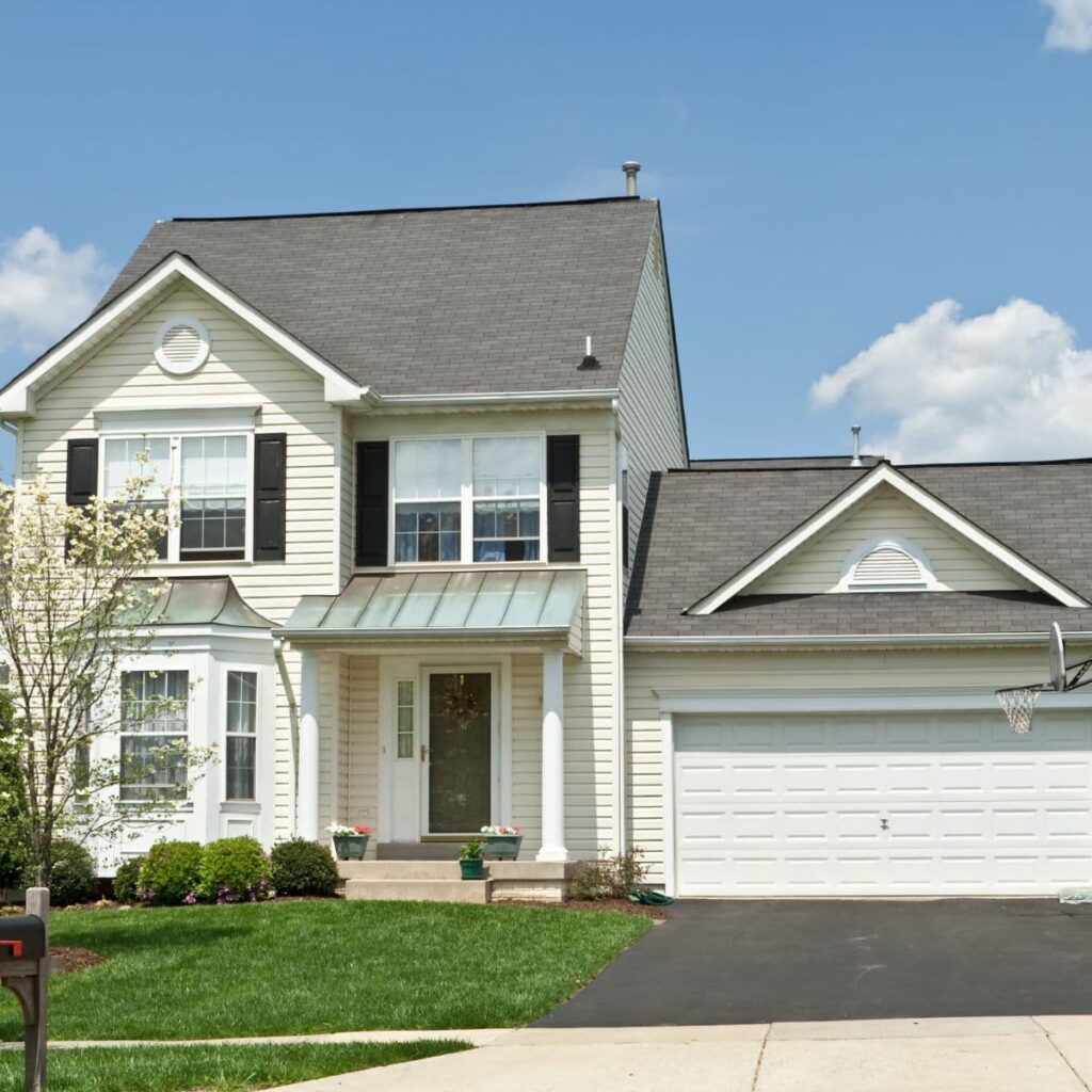 Beige two-story home with white columns, green metal awning, and a basketball hoop