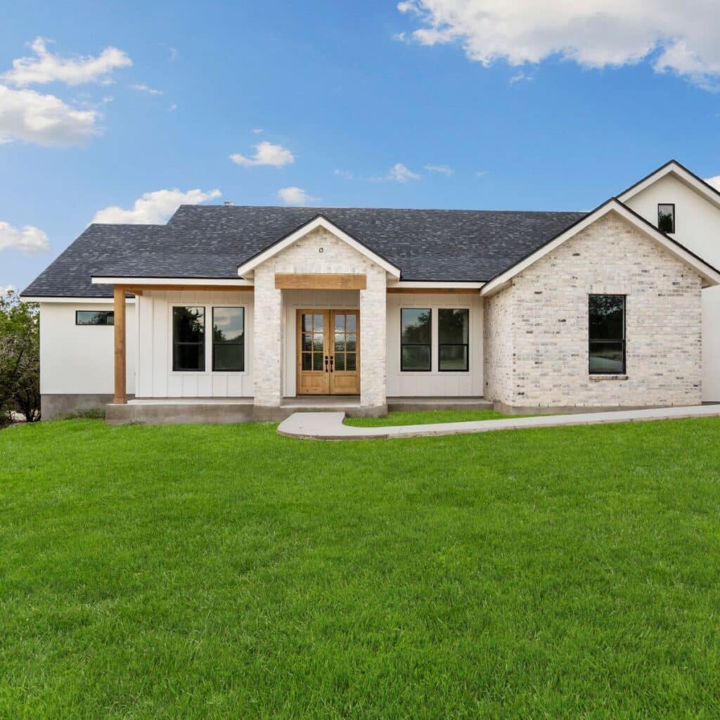 A charming farmhouse-style home with a mix of stone and board-and-batten siding, featuring a wooden front door and a lush green lawn