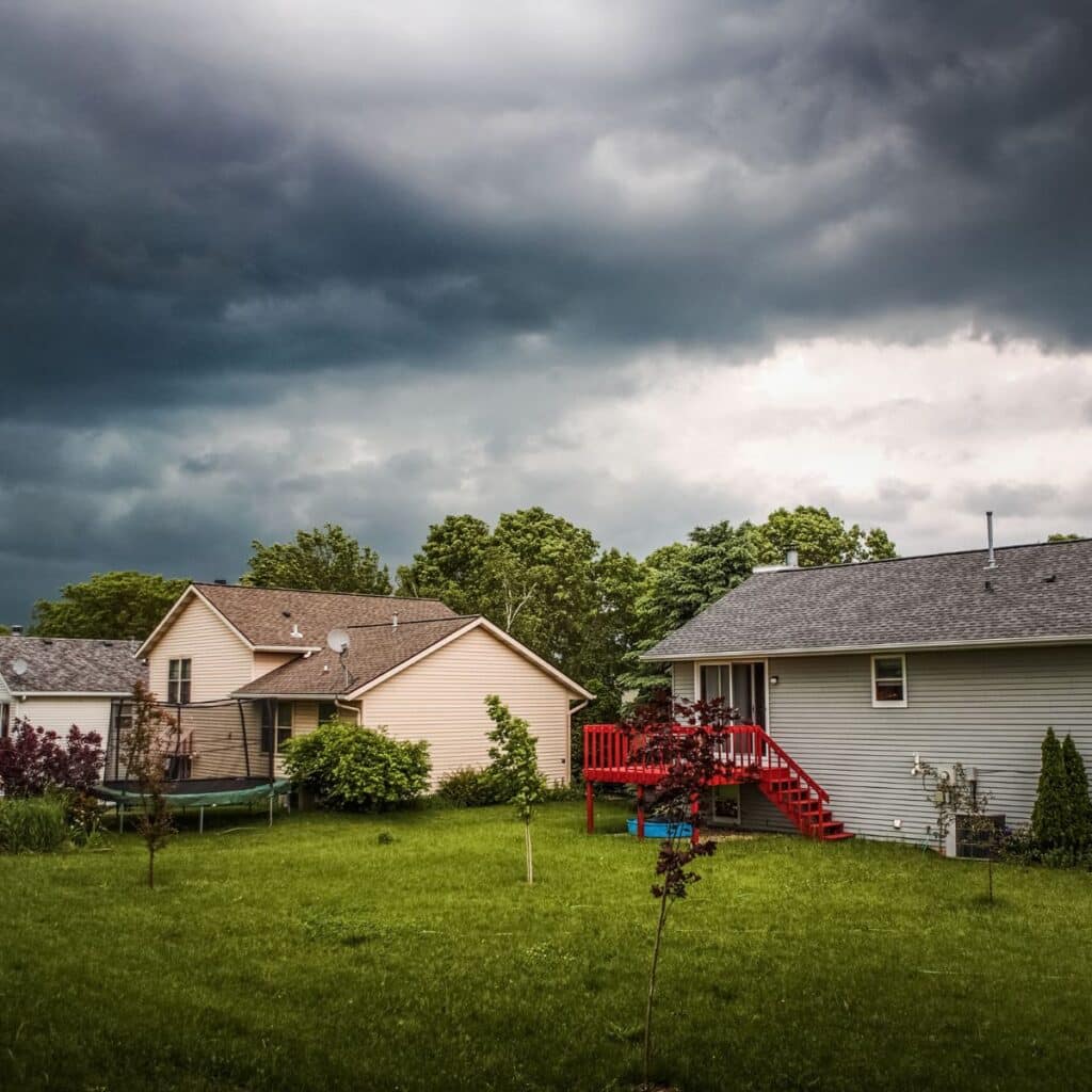 A row of suburban homes with storm clouds gathering above, suggesting an approaching thunderstorm