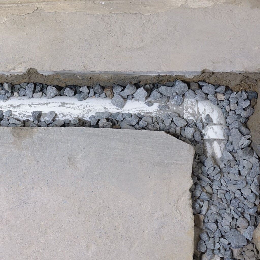 French drain system under concrete with gravel surrounding a white drainage pipe