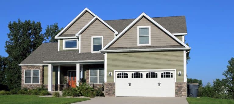 Two-story home with green and tan siding, stone accents, and a wide driveway