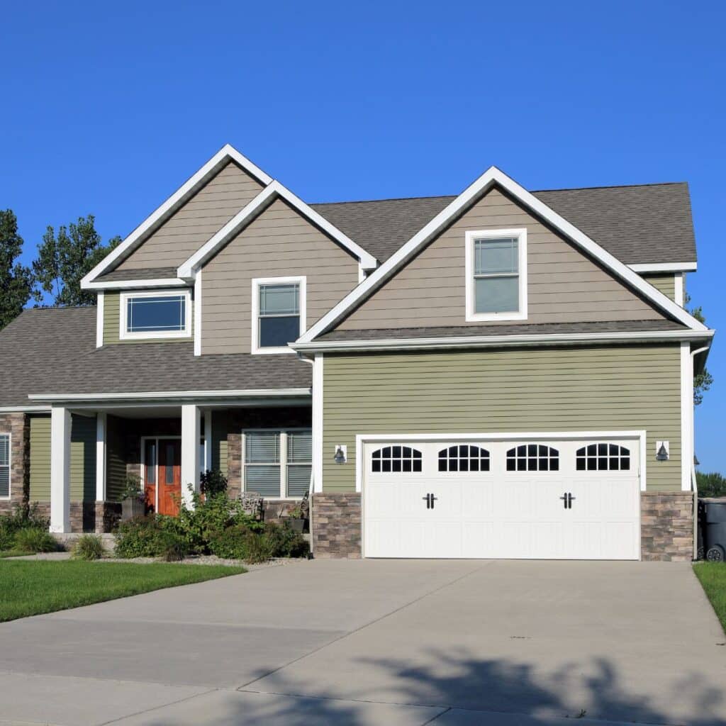 Two-story home with green and tan siding, stone accents, and a wide driveway