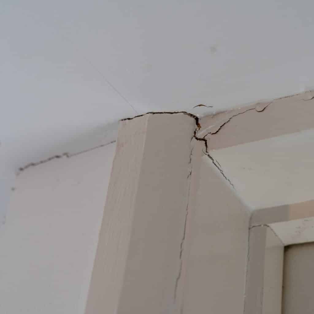 Severe, jagged cracks are visible where a light-colored wall meets a ceiling and doorframe, indicating structural issues