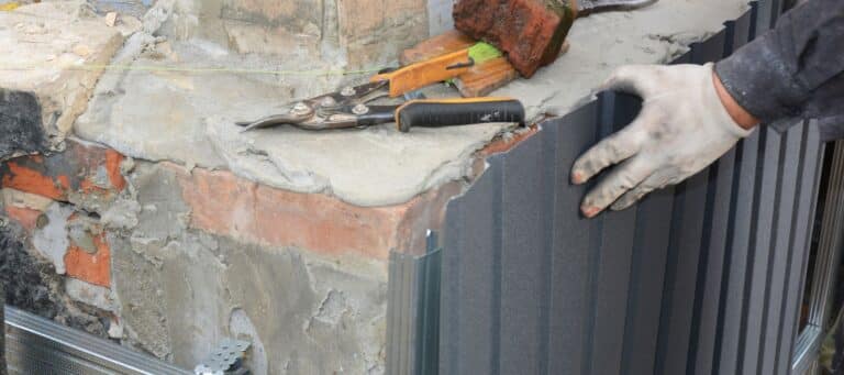Worker in gloves installing siding panels on a damaged brick foundation
