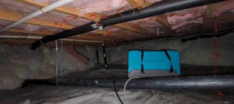 An encapsulated crawl space features a white vapor barrier on the ground, with pipes, wires, and a blue dehumidifier visible overhead