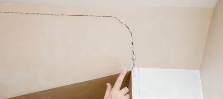 Hand pointing at a large crack running through an interior wall