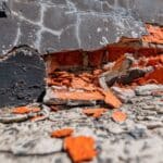Damaged foundation wall with exposed red brick and crumbling mortar