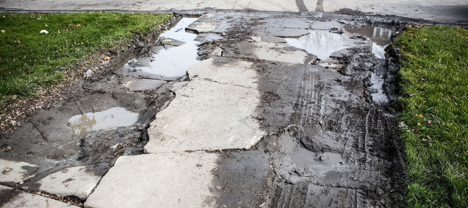 Damaged concrete sidewalk with standing water and mud