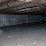 Dark crawl space under a house with exposed pipes and concrete block walls