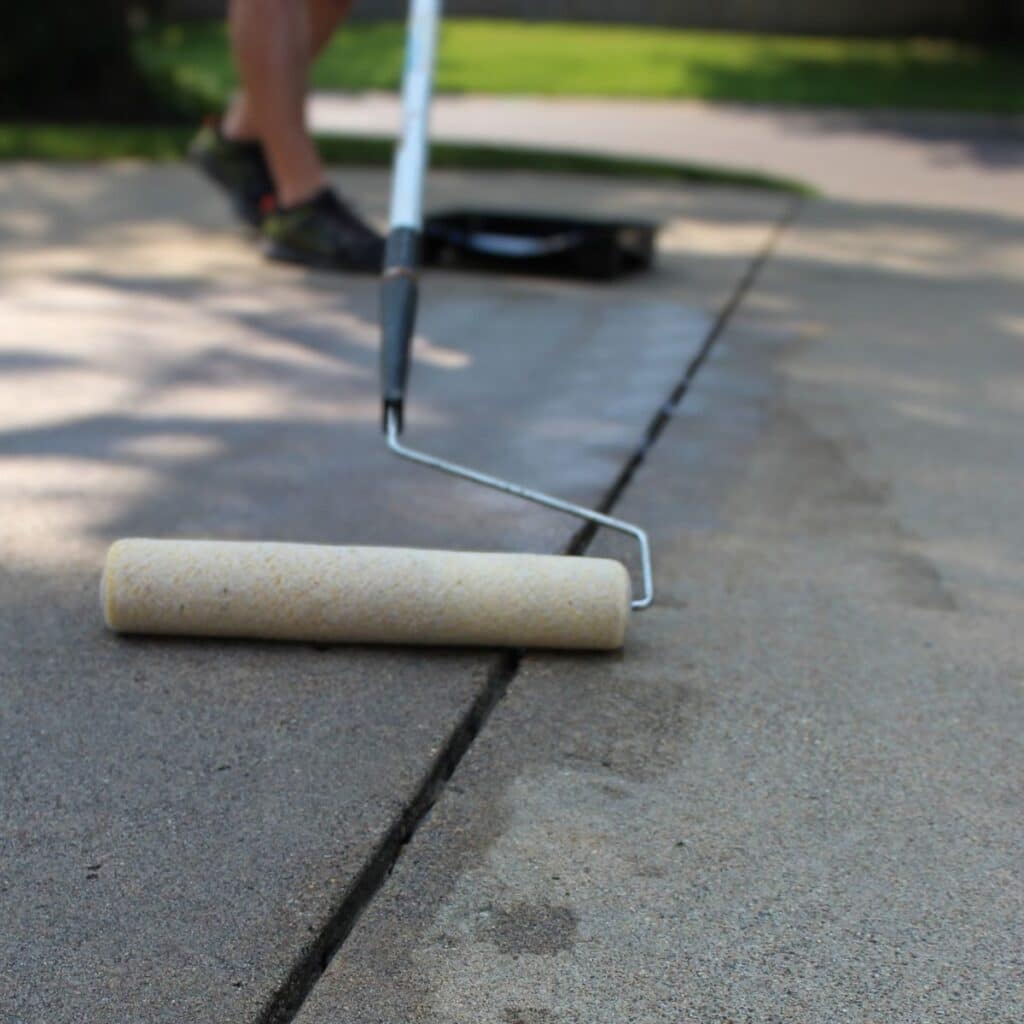 A paint roller applies sealant to a concrete surface