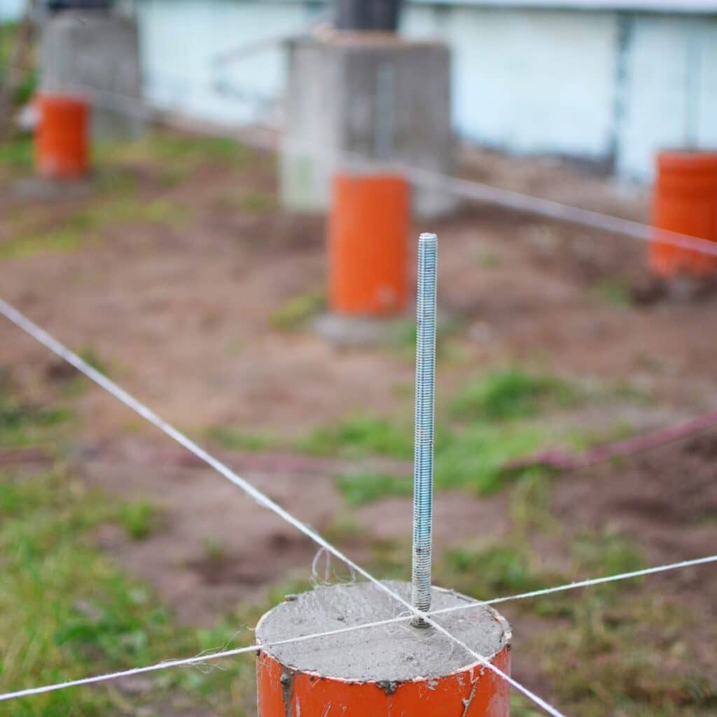 A steel piling with a central threaded rod set in concrete at a construction site