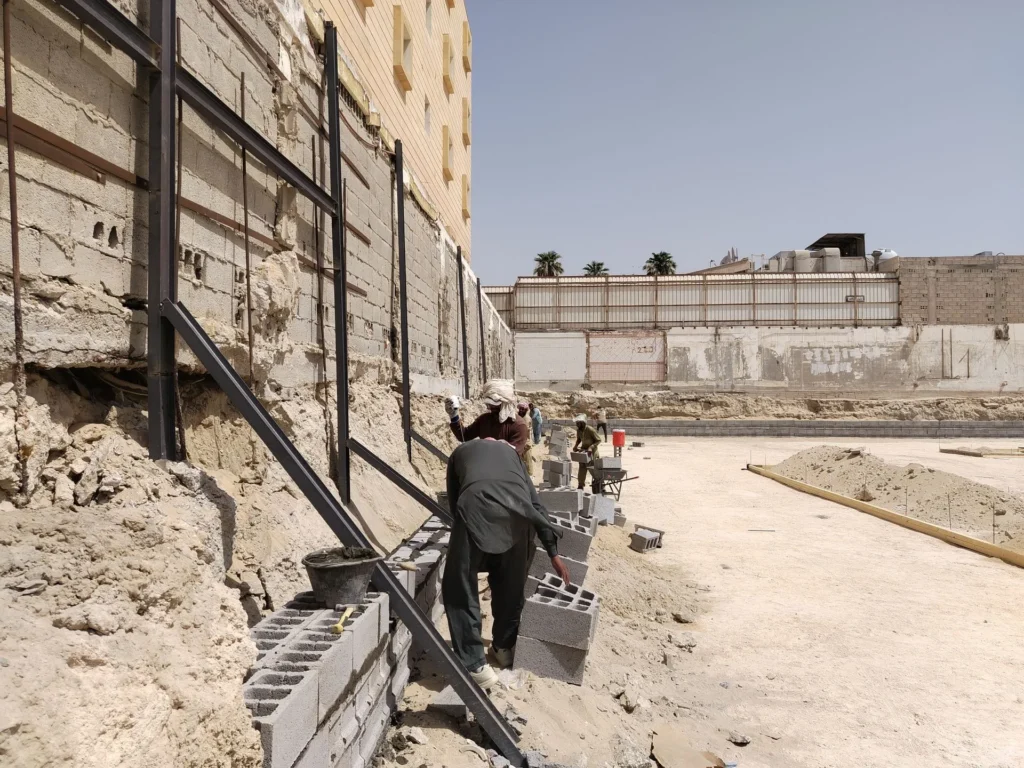 Workers laying concrete blocks during foundation wall construction at a building site.
