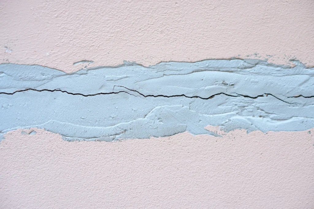 Hairline Cracks In Concrete wall surface with a visible horizontal fracture running through a repaired cement patch.