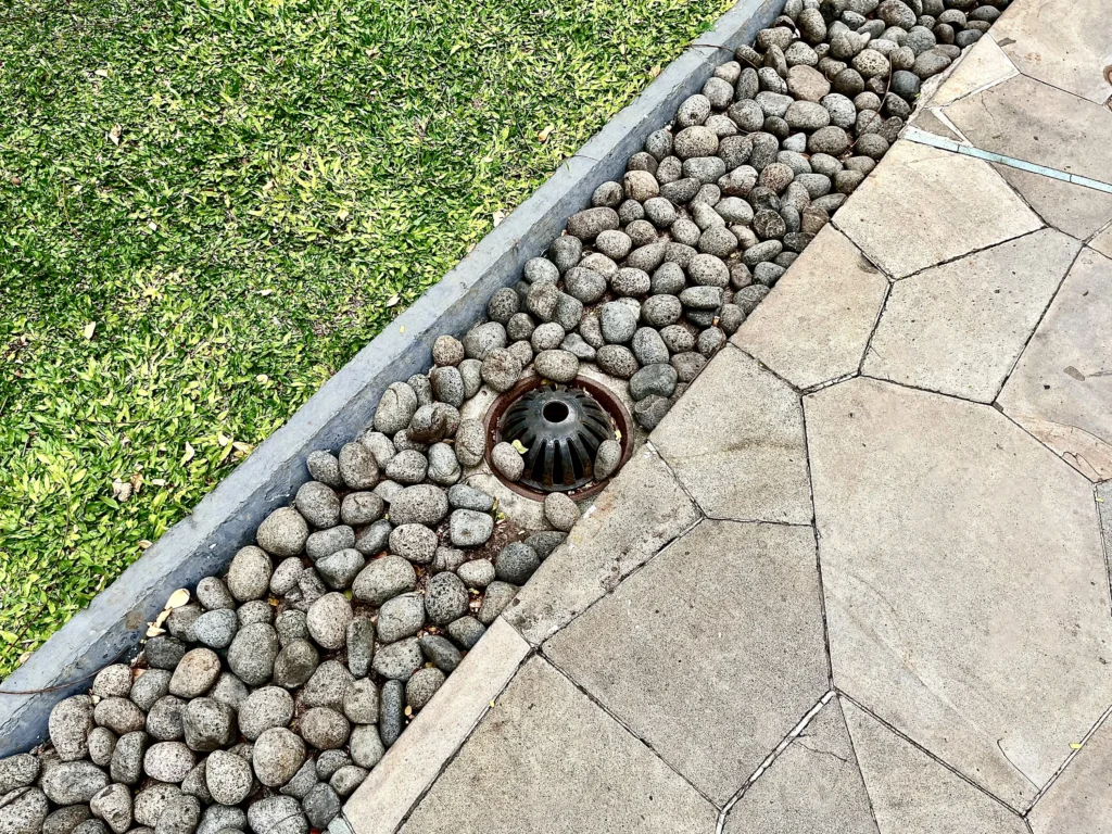 River rock French drain with catch basin beside a flagstone patio.