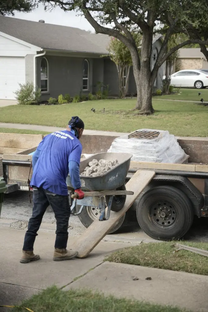  G.L. Hunt crew member wheels broken concrete up a ramp onto a work trailer outside a Texas home during foundation repair.